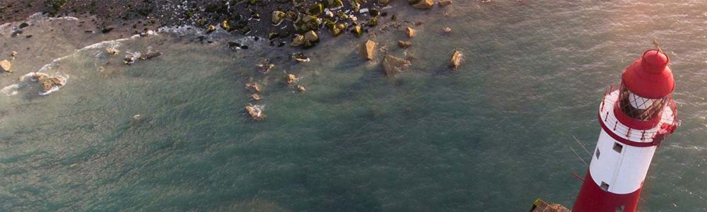 Ein Leuchtturm aus der Vogelperspektive in einer Bucht.