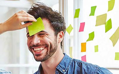 Ein Mann bekommt ein Post-It Zettel auf die Stirn geklebt (Workshops & Konferenzen zum Zukunftsunternehmen)