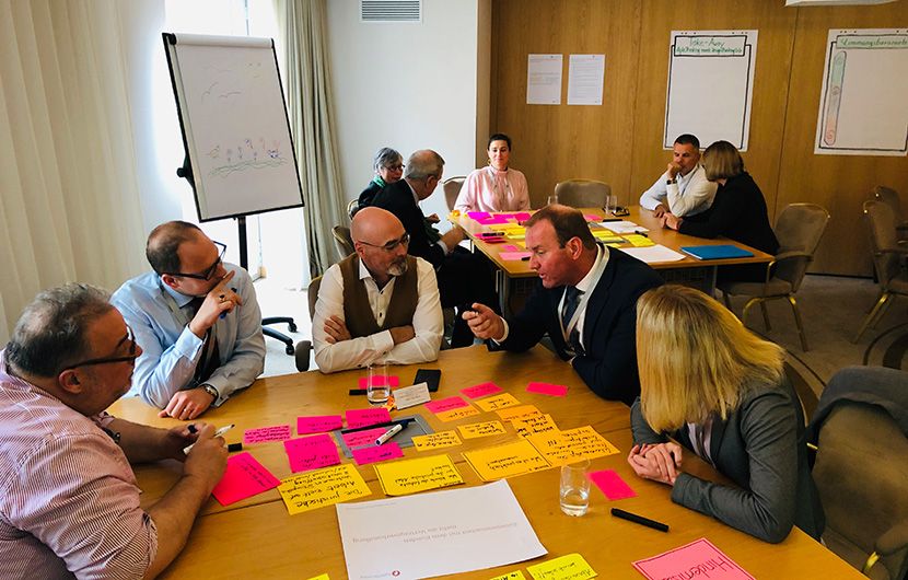 Zwei Gruppen sitzen jeweils an einem Tisch und führen eine Diskussion